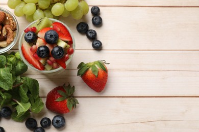 Photo of Delicious fruit salad in glass and ingredients on light wooden table, flat lay. Space for text