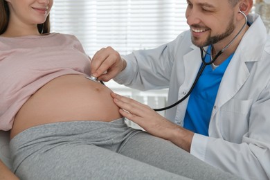 Doctor examining pregnant woman with stethoscope in clinic, closeup