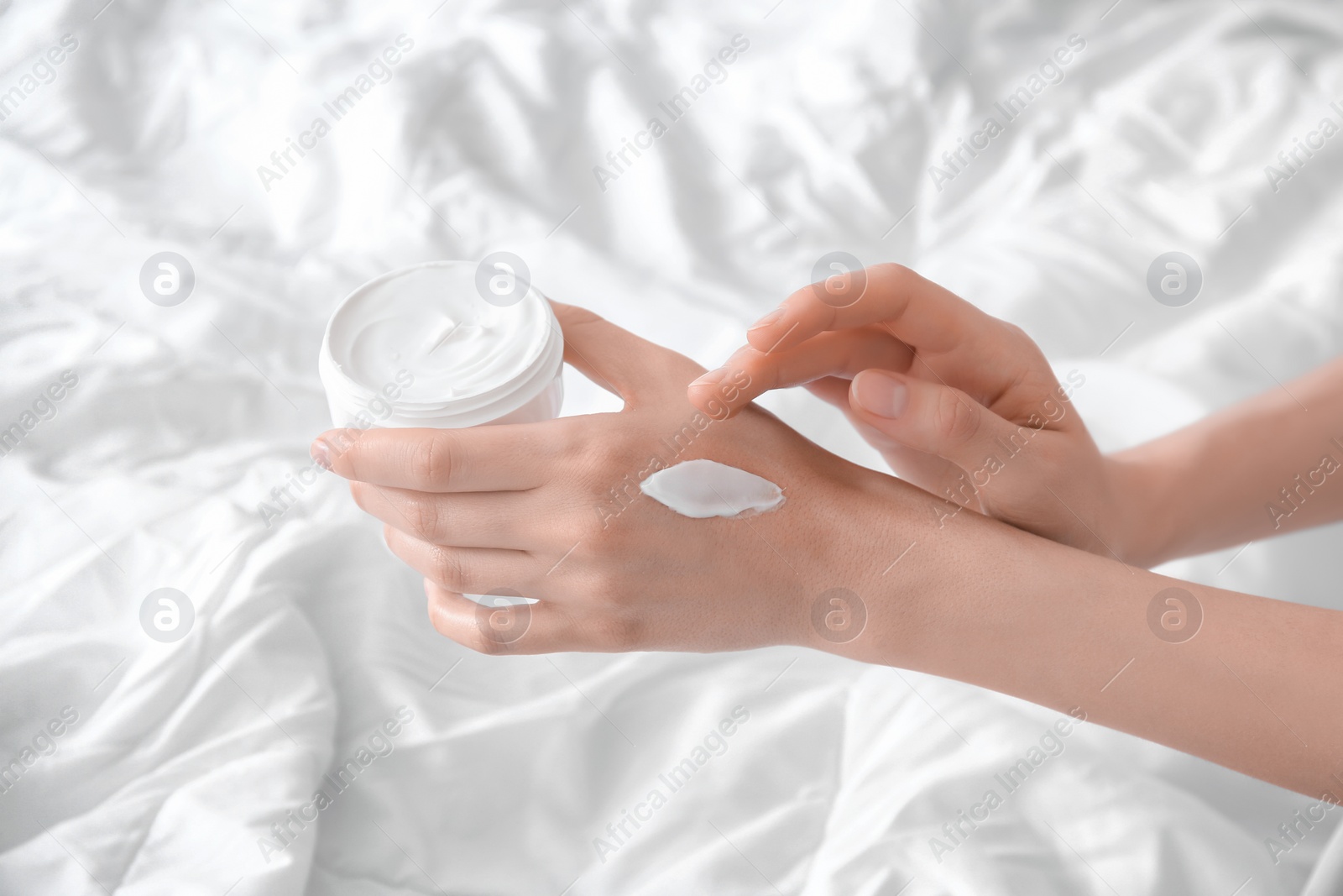 Photo of Young woman applying cream onto hands, indoors