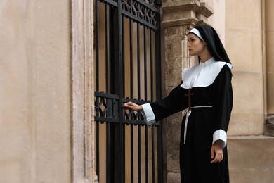 Photo of Young nun in cassock near metal door outdoors