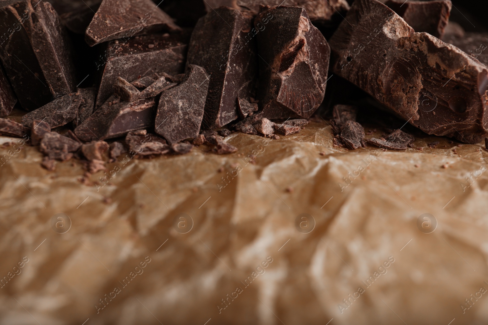 Photo of Pieces of dark chocolate on parchment, closeup. Space for text
