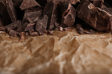 Pieces of dark chocolate on parchment, closeup. Space for text