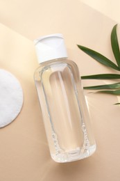 Photo of Micellar water and cotton pad on beige background, flat lay