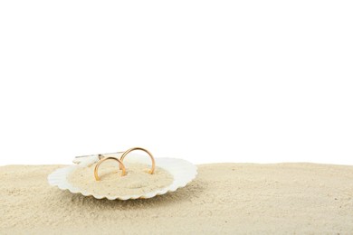 Photo of Honeymoon concept. Two golden rings in shell and sand isolated on white