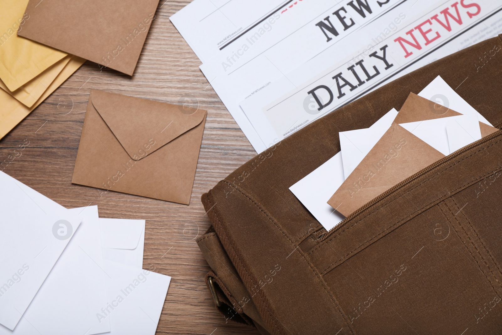 Photo of Postman bag, newspapers and mails on wooden table, flat lay