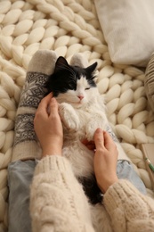 Woman stroking adorable cat on knitted blanket, closeup