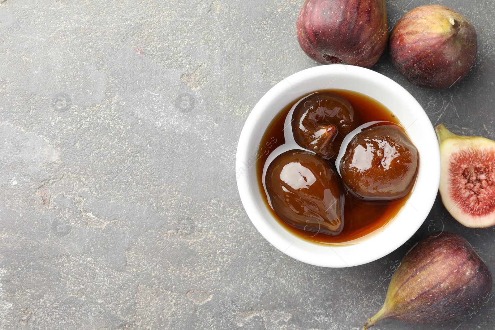 Photo of Bowl of tasty sweet jam and fresh figs on grey table, flat lay. Space for text