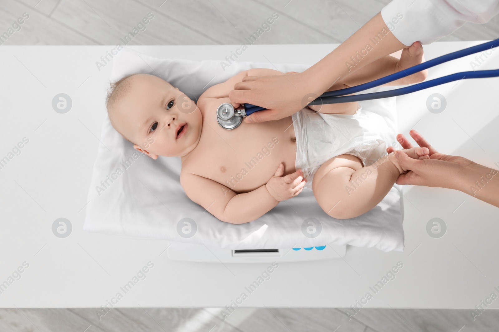 Photo of Pediatrician weighting and examining cute little baby with stethoscope in clinic, closeup