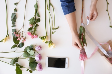 Female florist creating beautiful bouquet at table, top view