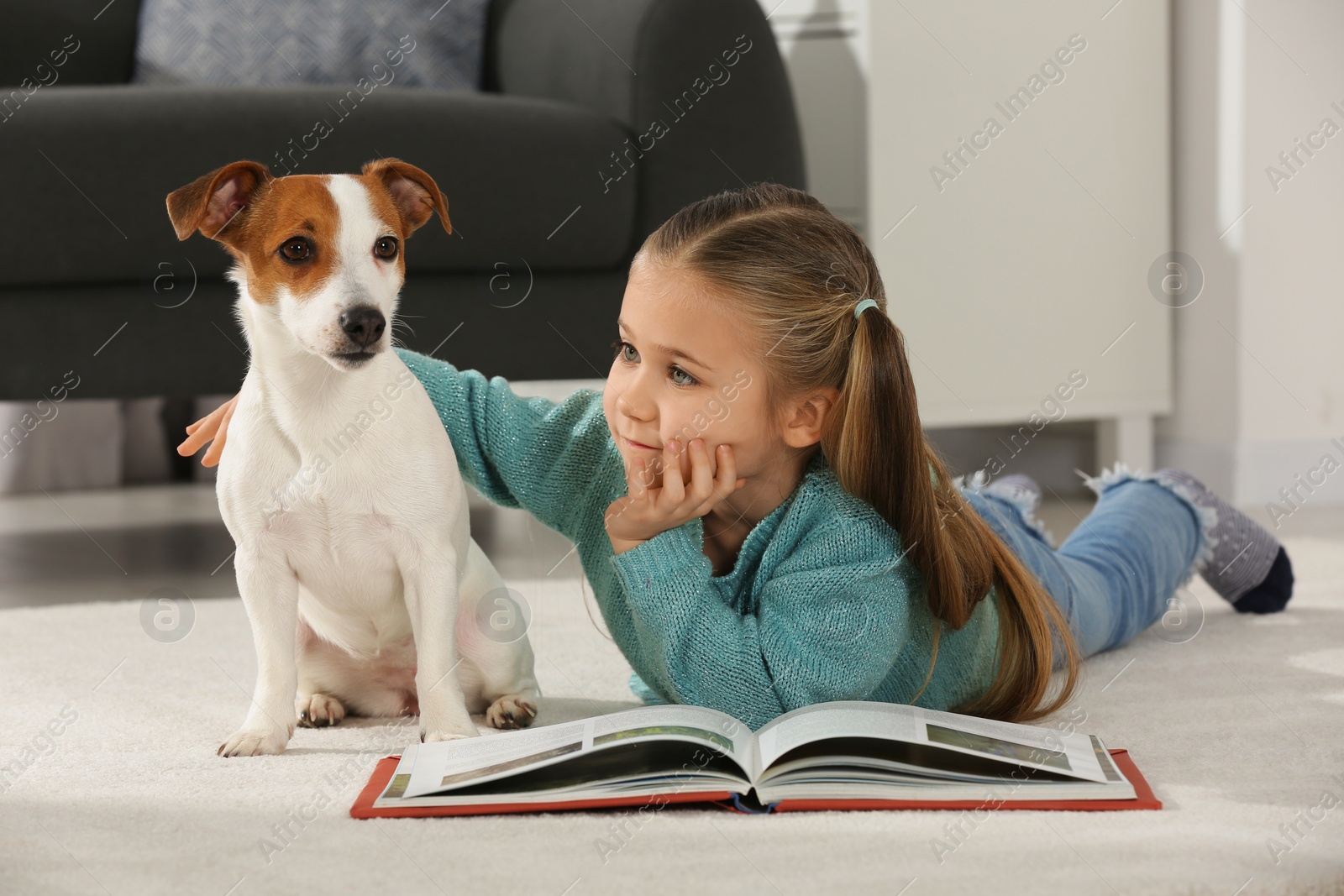 Photo of Cute girl reading book on floor with her dog at home. Adorable pet