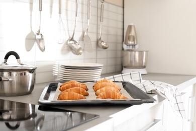 Oven sheet with freshly baked croissants on kitchen counter