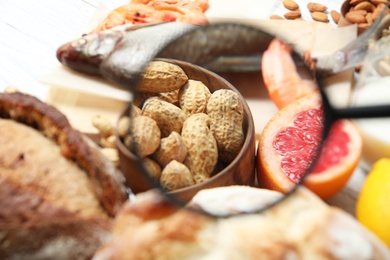 Different products with magnifier focused on peanuts and grapefruit, closeup. Food allergy concept