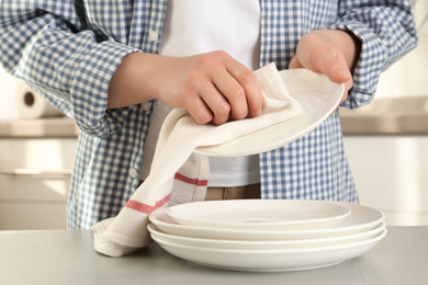 Photo of Woman wiping plate with towel at light grey table in kitchen, closeup