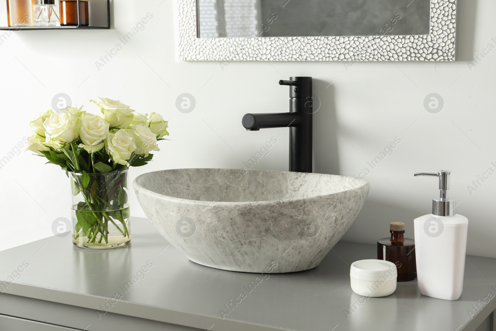 Photo of Vase with beautiful white roses and toiletries near sink in bathroom