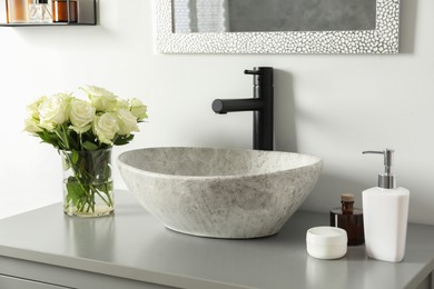 Vase with beautiful white roses and toiletries near sink in bathroom