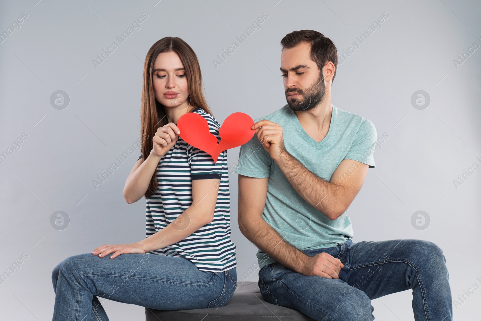 Photo of Couple tearing paper heart on light grey background. Relationship problems