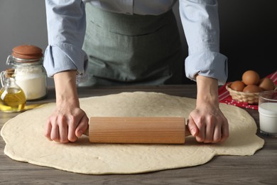 Photo of Woman rolling raw dough at wooden table, closeup