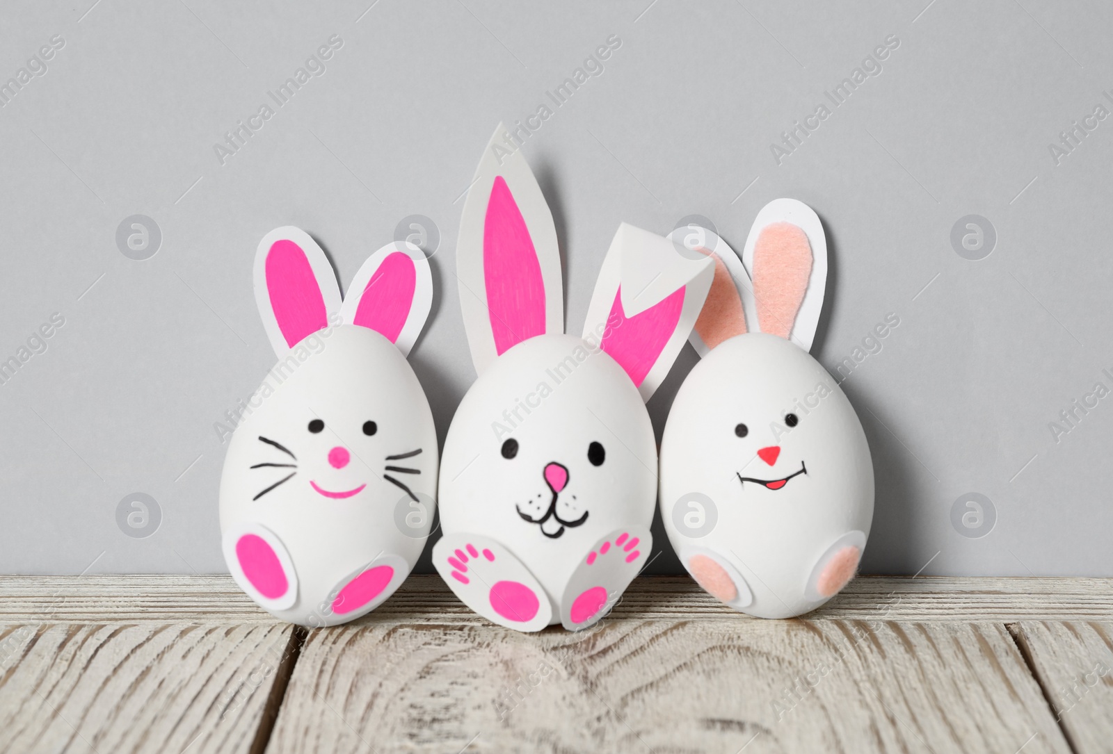 Photo of Eggs as cute bunnies on white wooden table against light grey background. Easter celebration