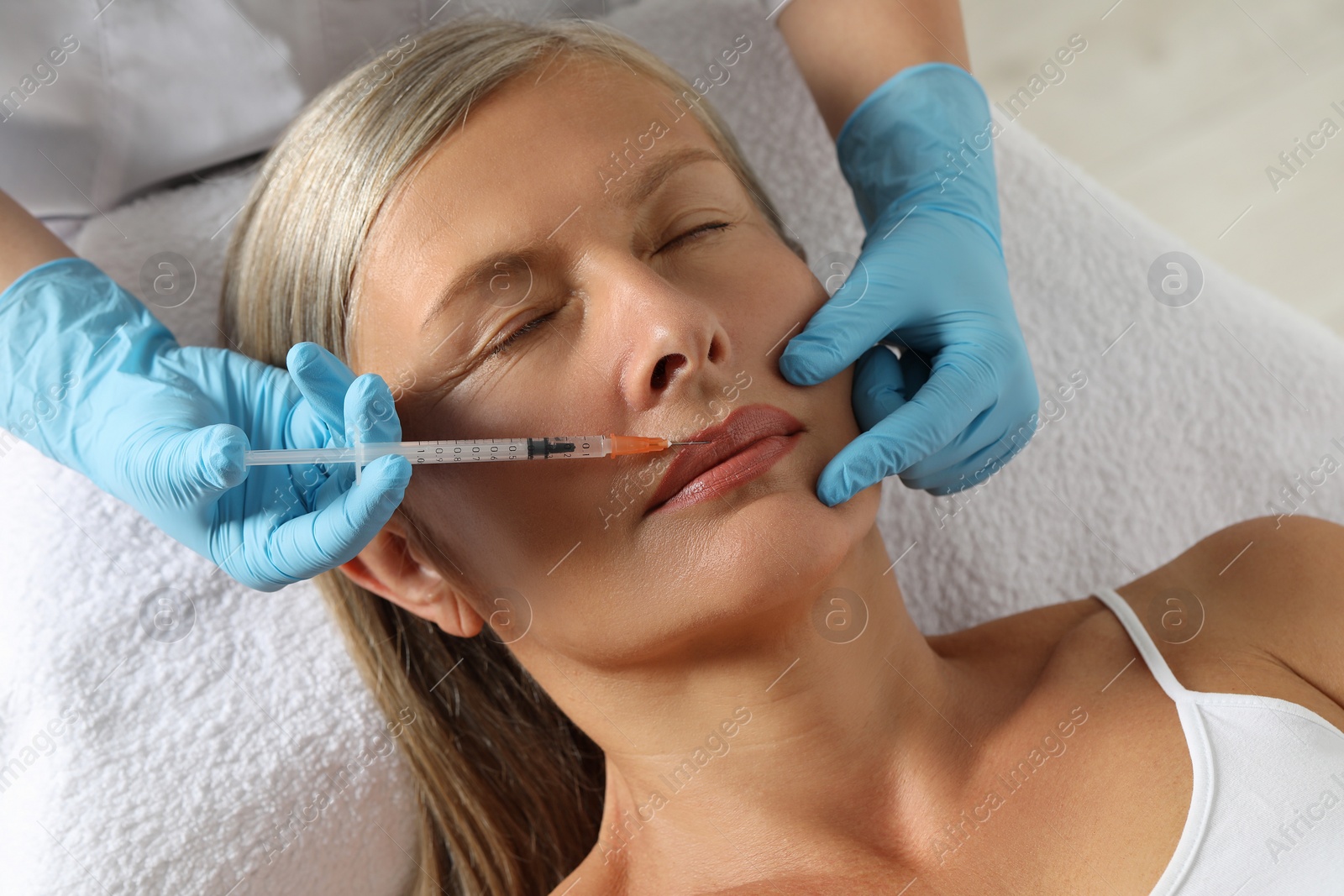 Photo of Doctor giving lips injection to senior woman in clinic. Cosmetic surgery