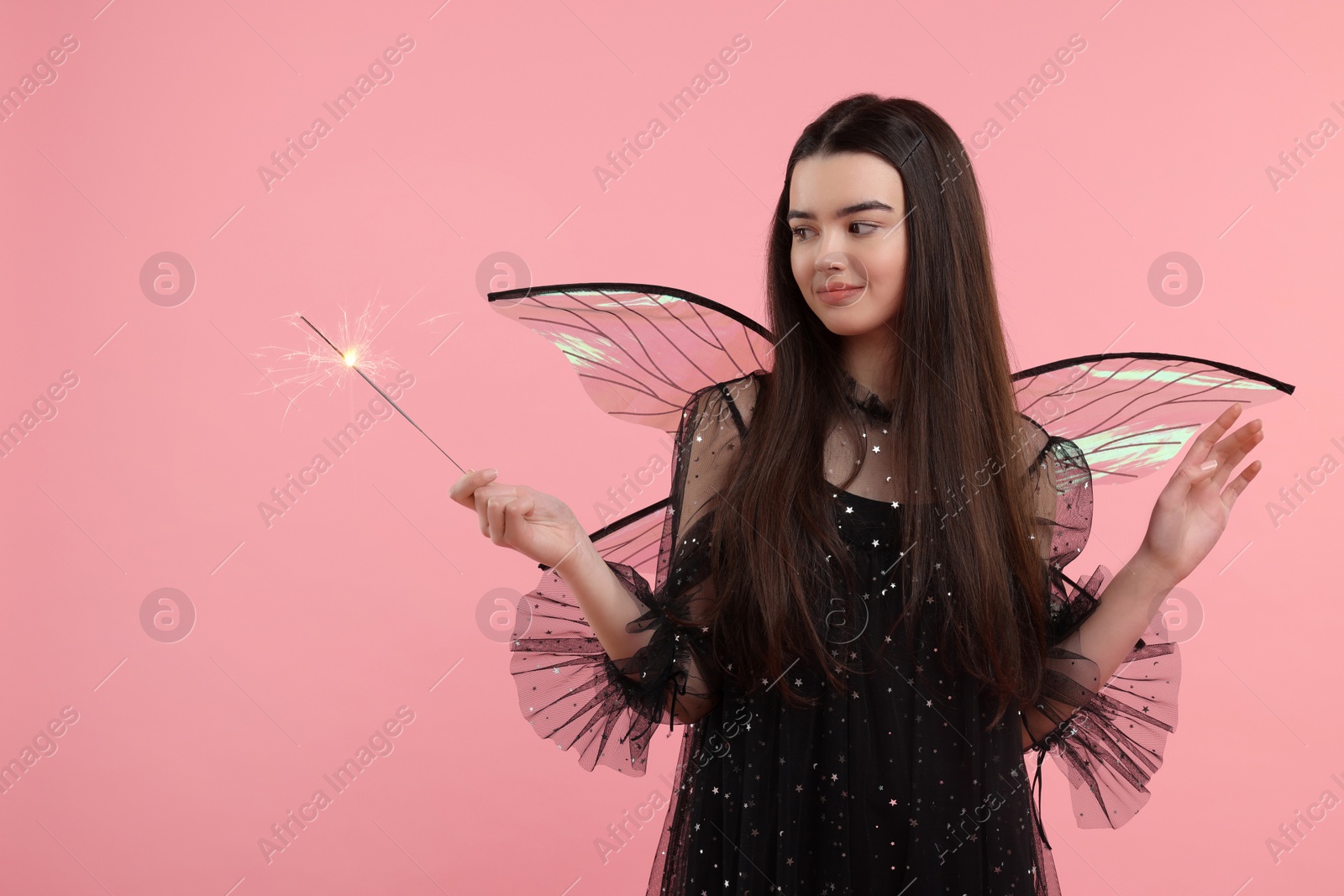 Photo of Beautiful girl in fairy costume with wings and magic wand on pink background