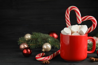 Photo of Cup of tasty cocoa with marshmallows, candy canes and Christmas decor on black wooden table. Space for text