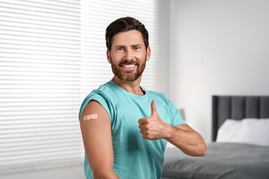 Photo of Man with sticking plaster on arm after vaccination showing thumbs up in bedroom
