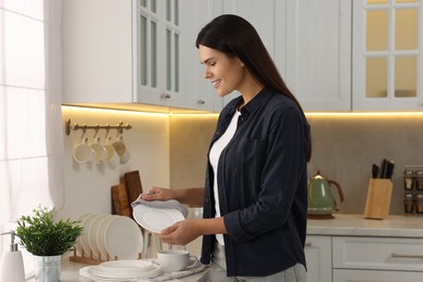 Photo of Happy woman wiping plate with towel in kitchen