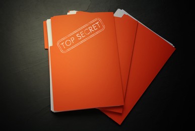 Orange file with documents and Top Secret stamp on black table, flat lay