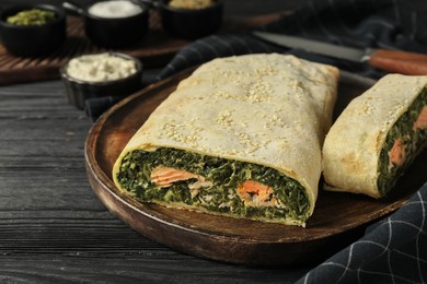 Photo of Tasty strudel with salmon and spinach on black wooden table, closeup