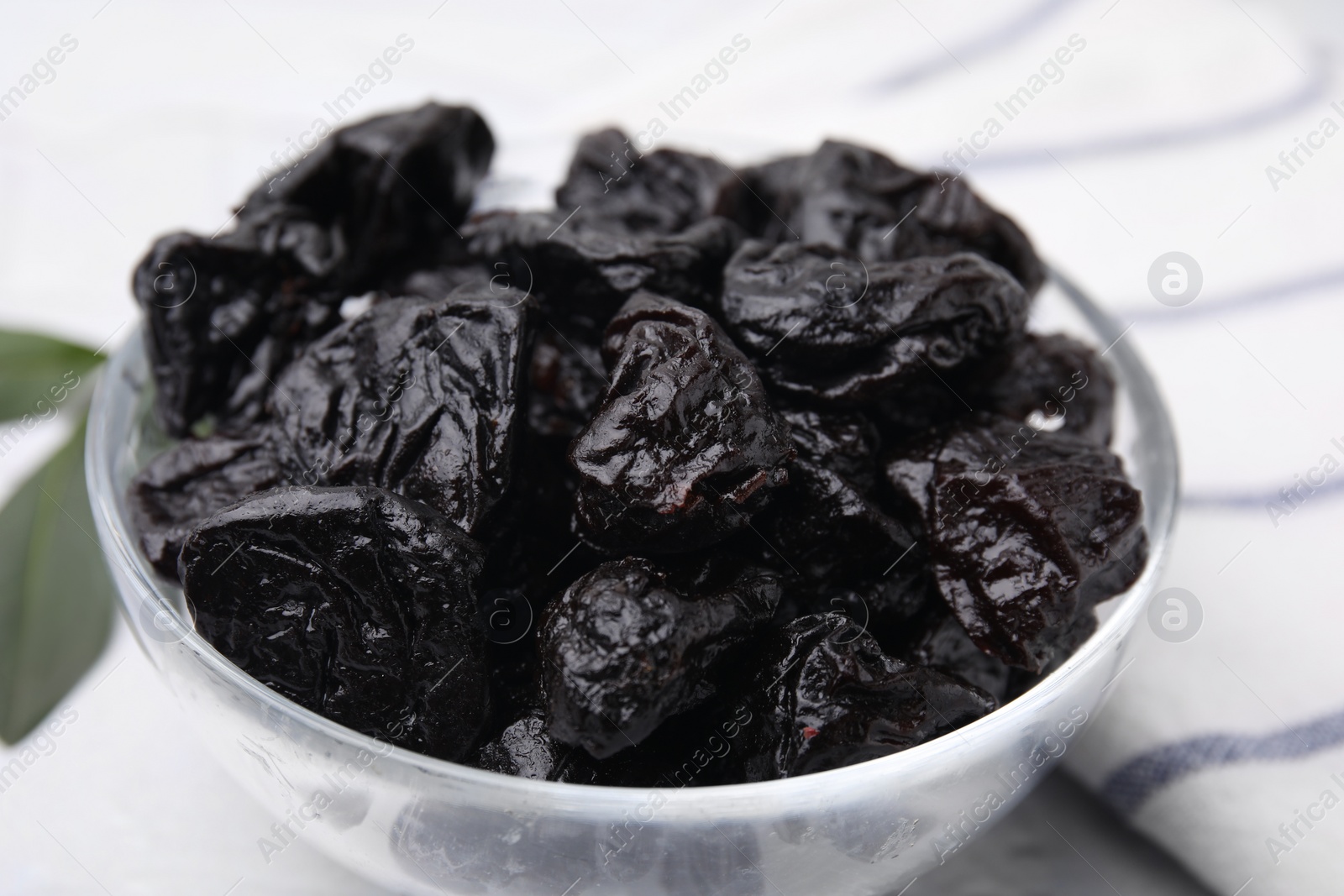 Photo of Sweet dried prunes in bowl on light table, closeup