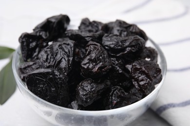 Sweet dried prunes in bowl on light table, closeup