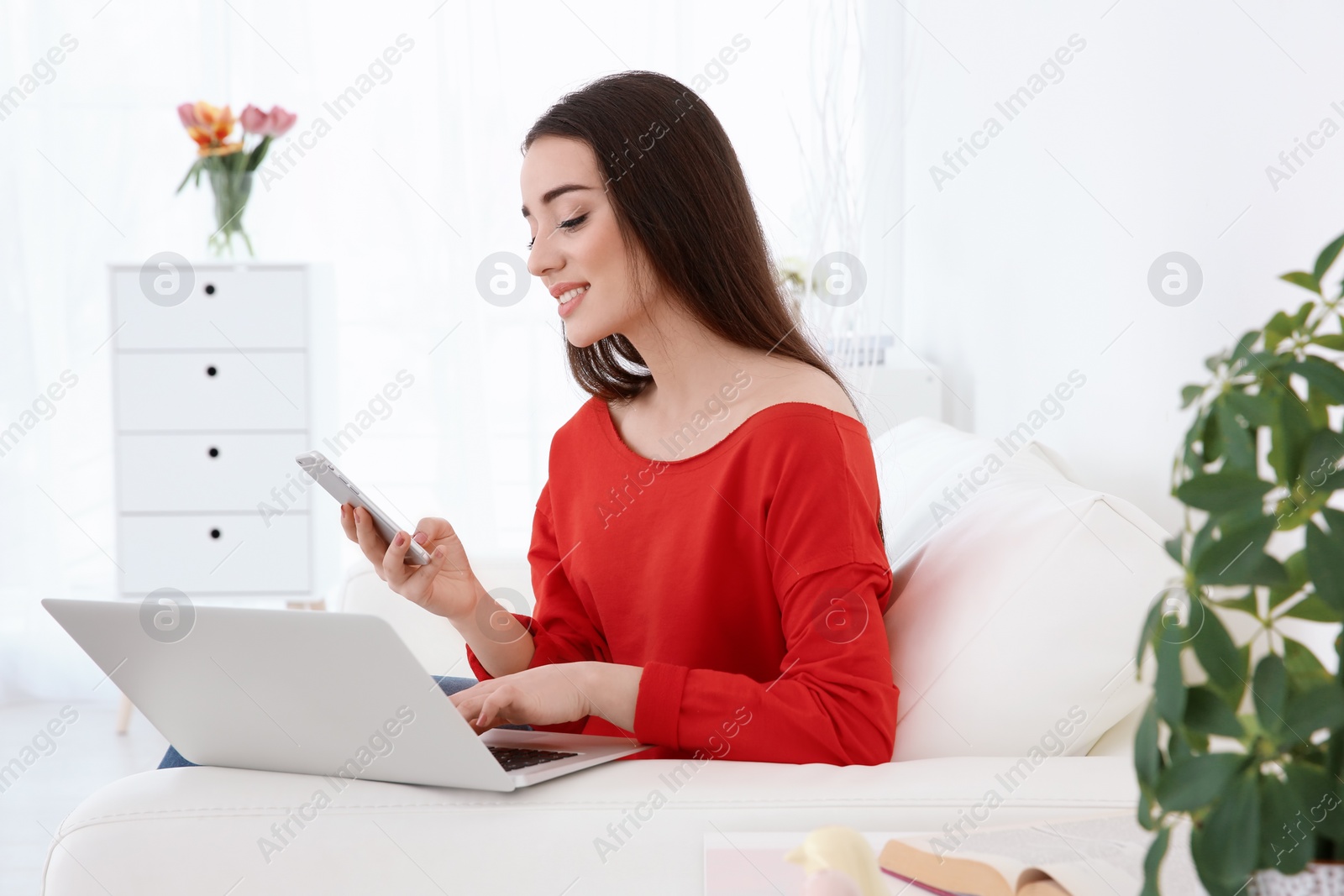 Photo of Attractive young woman using mobile phone and laptop at home