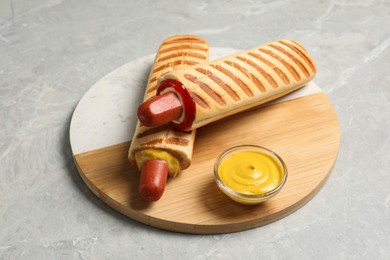 Photo of Tasty french hot dogs and dip sauce on light grey marble table