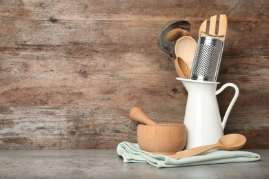 Different kitchen utensils on grey table against wooden background. Space for text