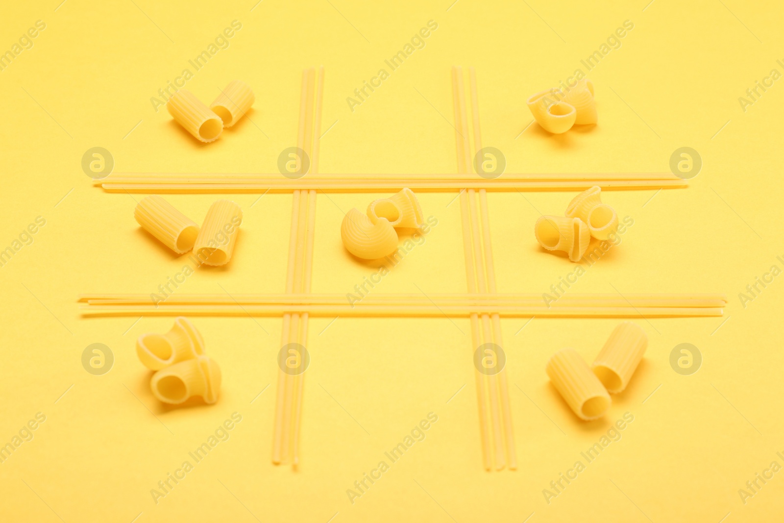 Photo of Tic tac toe game made with different types of pasta on yellow background