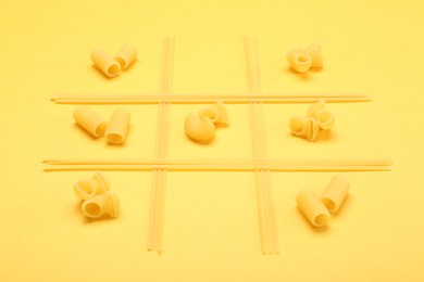 Photo of Tic tac toe game made with different types of pasta on yellow background