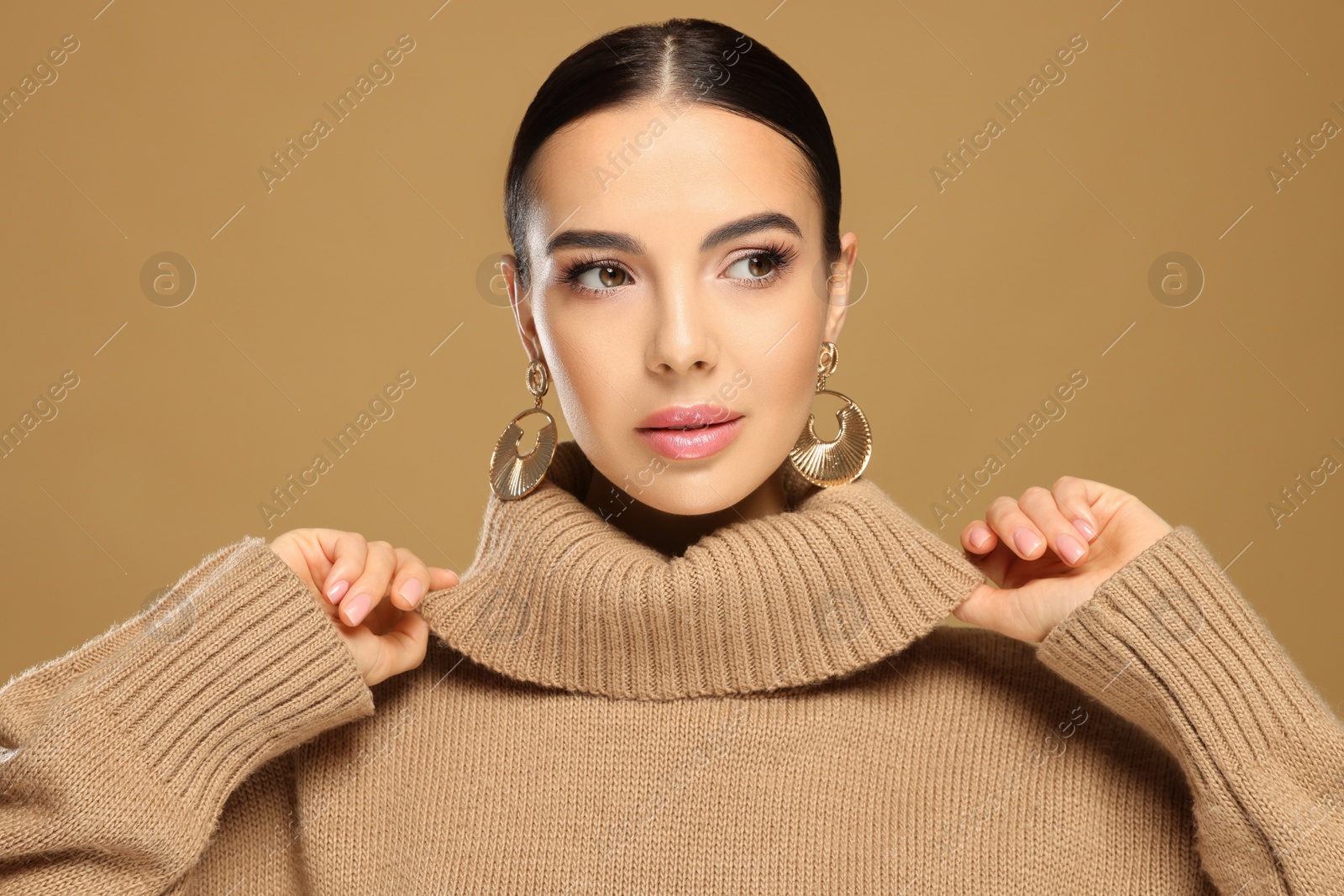 Photo of Beautiful young woman with elegant earrings on light brown background