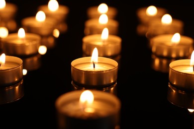 Burning candles on mirror surface in darkness, closeup