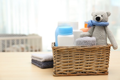 Wicker basket with baby cosmetic products, toy and towels on table indoors. Space for text