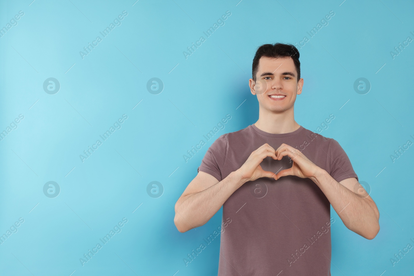 Photo of Happy volunteer making heart with his hands on light blue background. Space for text