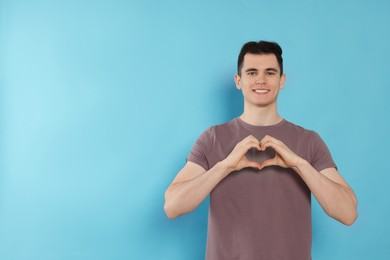 Happy volunteer making heart with his hands on light blue background. Space for text