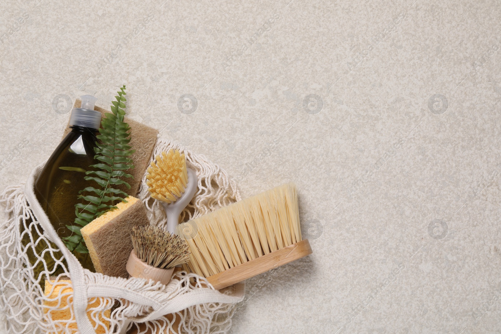 Photo of Different cleaning supplies in string bag on beige background, top view. Space for text