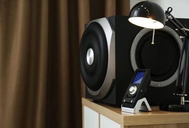 Photo of Modern subwoofer, remote and lamp on cabinet indoors, space for text. Powerful audio speaker