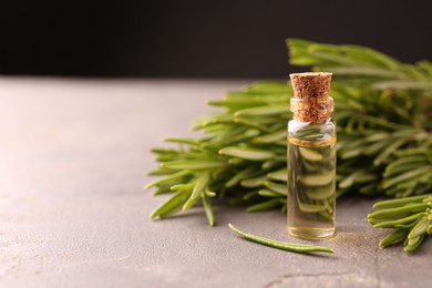 Photo of Essential oil in bottle and rosemary on grey table, space for text