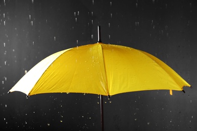 Photo of Bright umbrella under rain on dark background