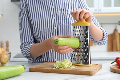 Photo of Woman grating zucchini at kitchen table, closeup