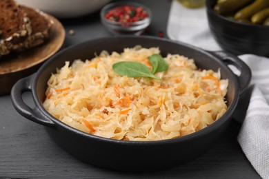 Photo of Serving pan with sauerkraut and products on black wooden table