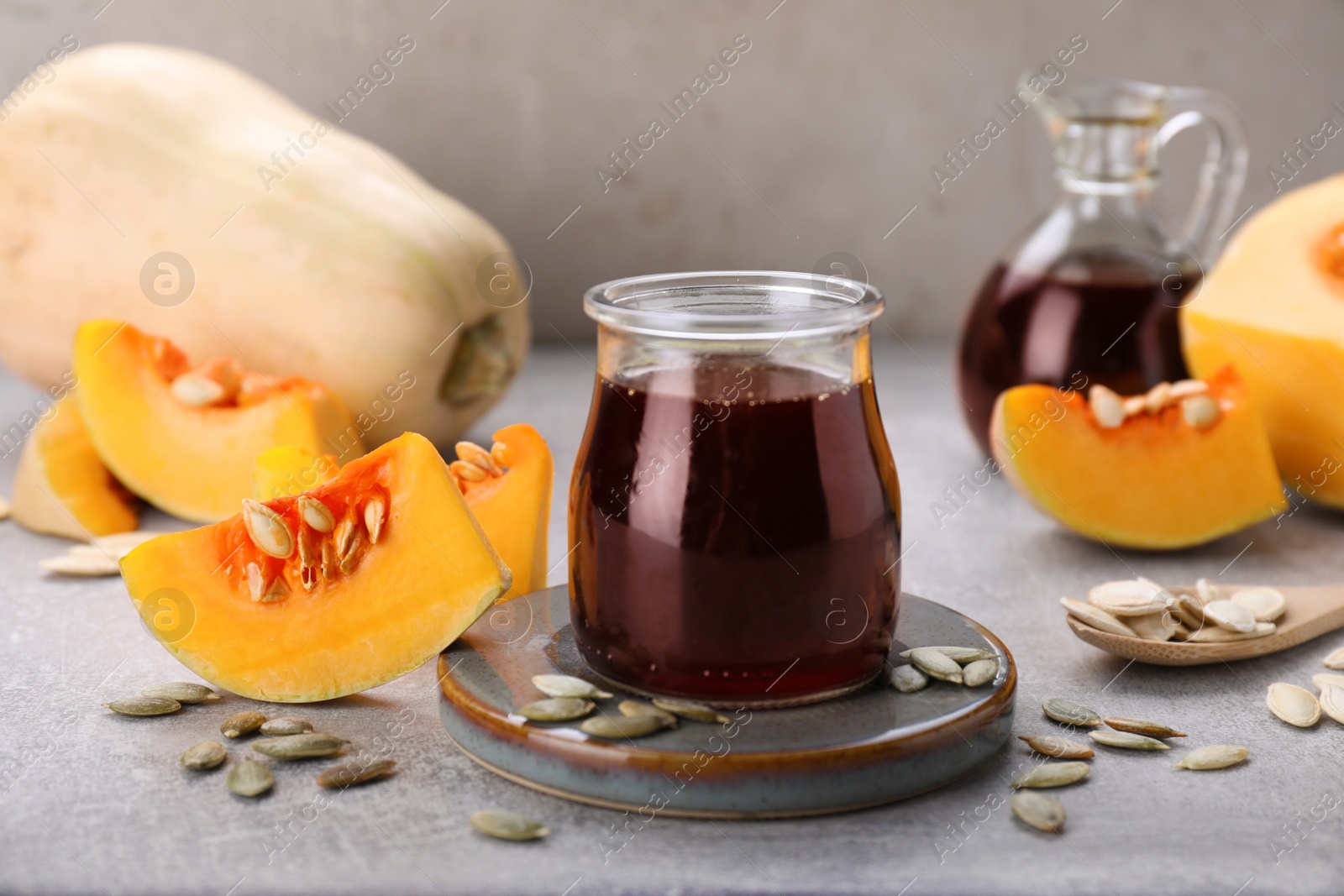 Photo of Fresh pumpkin seed oil in glass jar on grey table