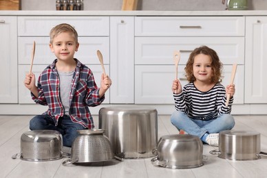 Photo of Little children pretending to play drums on pots in kitchen