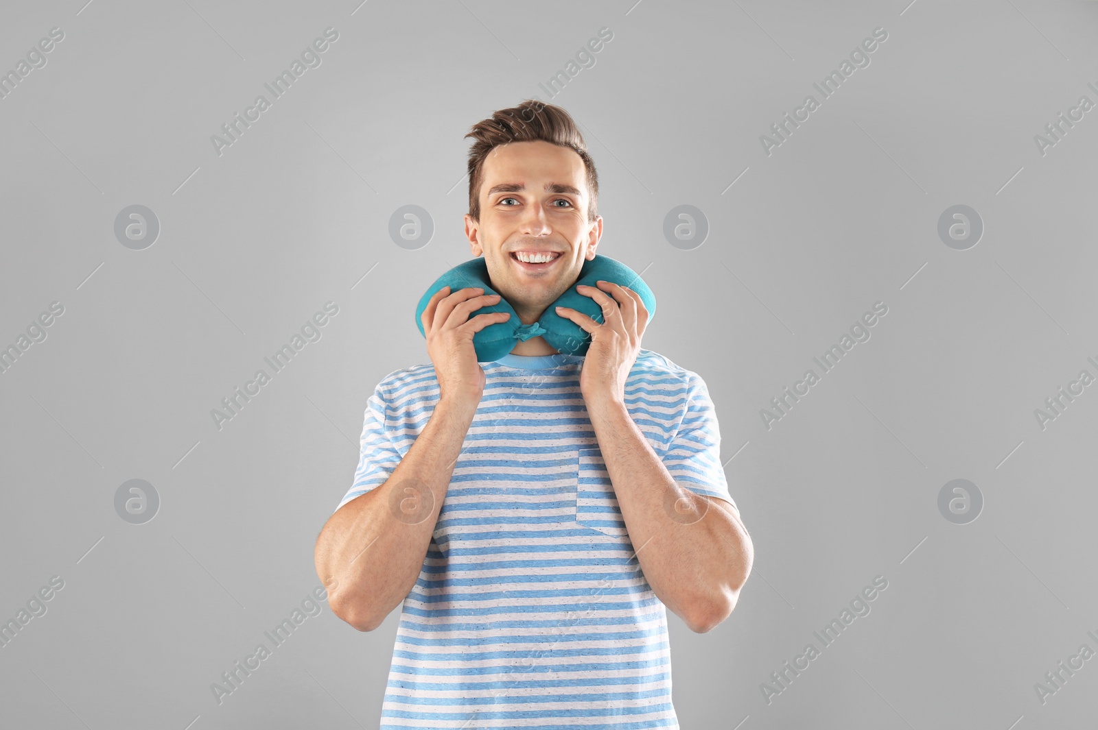 Photo of Happy young man with neck pillow on gray background